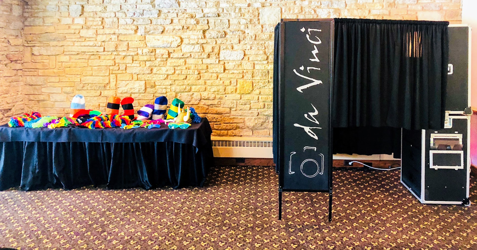Da Vinci enclosed photobooth with tower, curtains, and props table against a stone wall